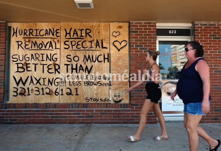 Dos mujeres caminan frente a un negocio cerrado y con sus ventanas aseguradas. (Foto: AFP)