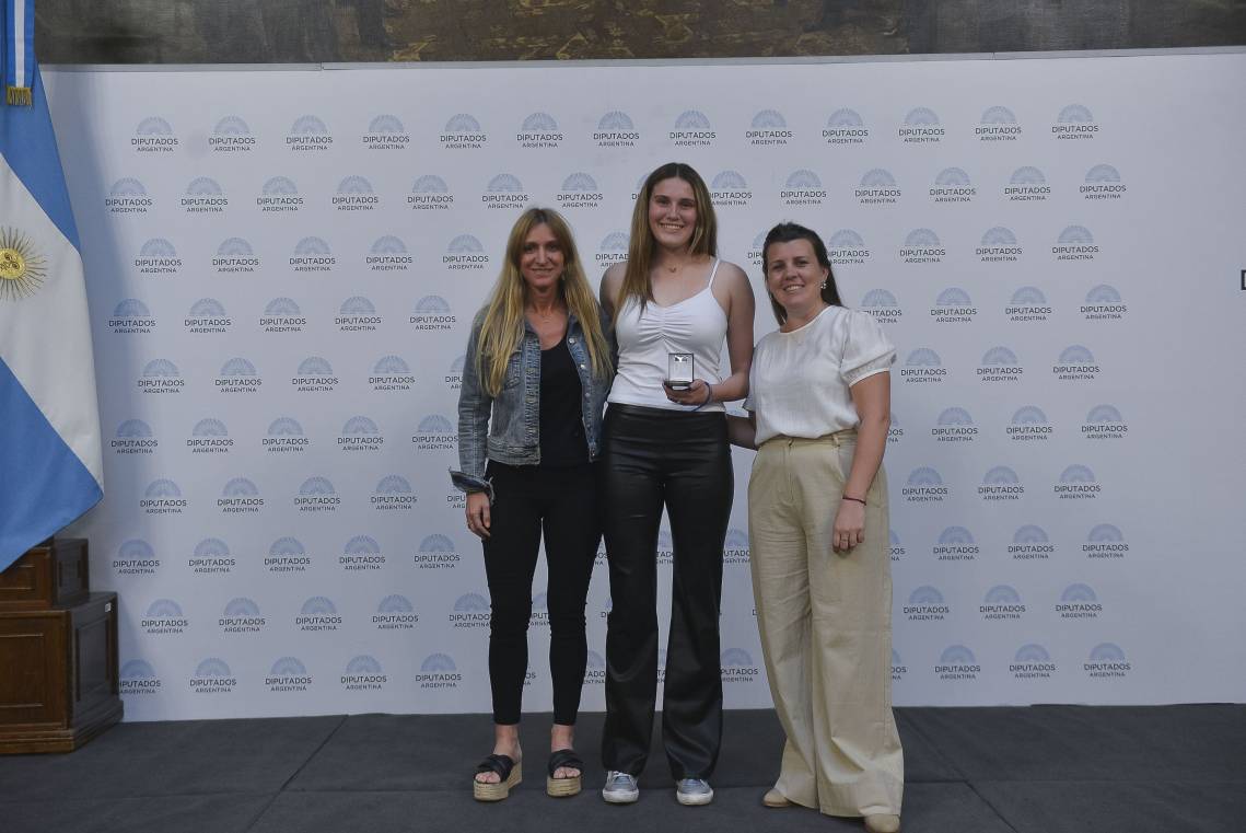 Emma Oldani recibiendo la medalla que la distingue con el premio Islas Malvinas de manos de las diputadas Magalí Mastaler y Florencia Carignano.