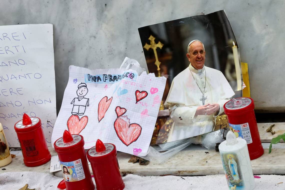 Una foto del Papa Francisco se observa junto a velas y dibujos en la base de la estatua del fallecido Papa Juan Pablo II, mientras el pontífice argentino continúa su tratamiento en el hospital Gemelli, en Roma.