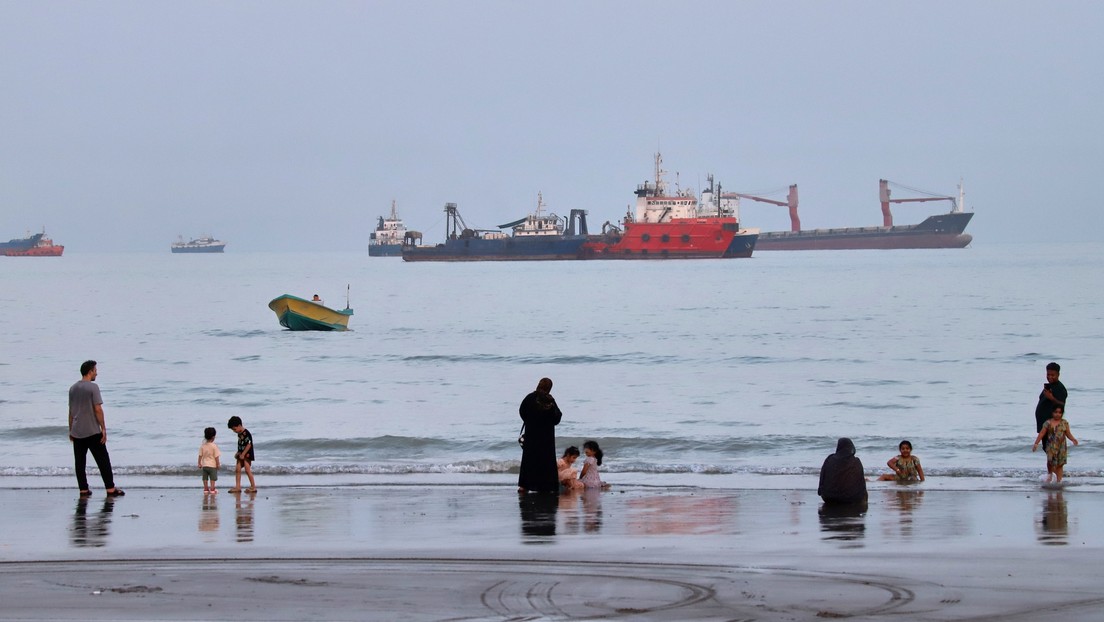 Personas pasan tiempo en una playa mientras buques comerciales permanecen anclados en el estrecho de Ormuz. (Crédito:  Amirhosein Khorgooi / ISNA / AP)